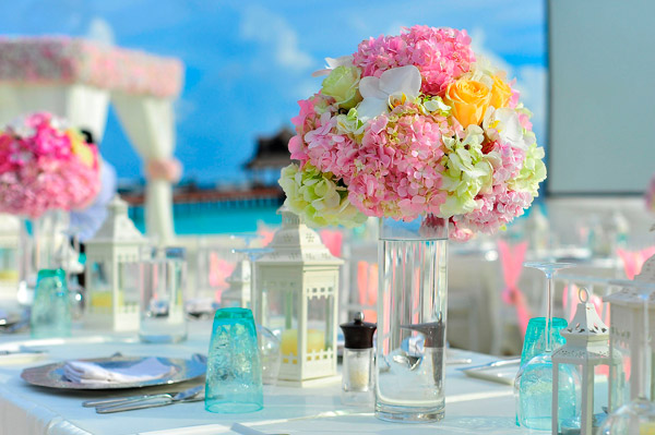 Decoração de casamento na praia mostrando lindos arranjos redondos de flores coloridas e uma tenda branca ao fundo.